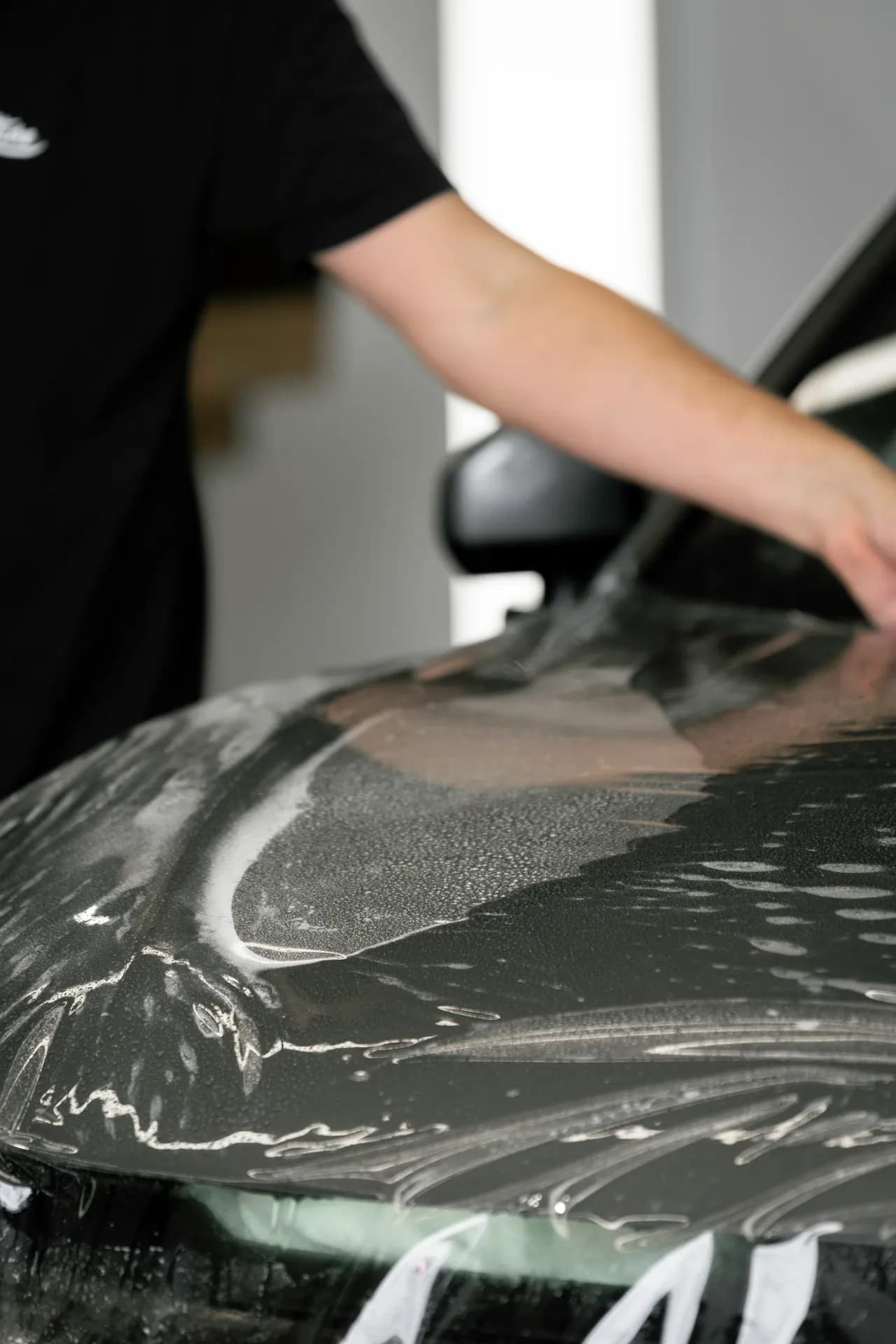 Close-up of paint protection film being applied to a dark vehicle bonnet