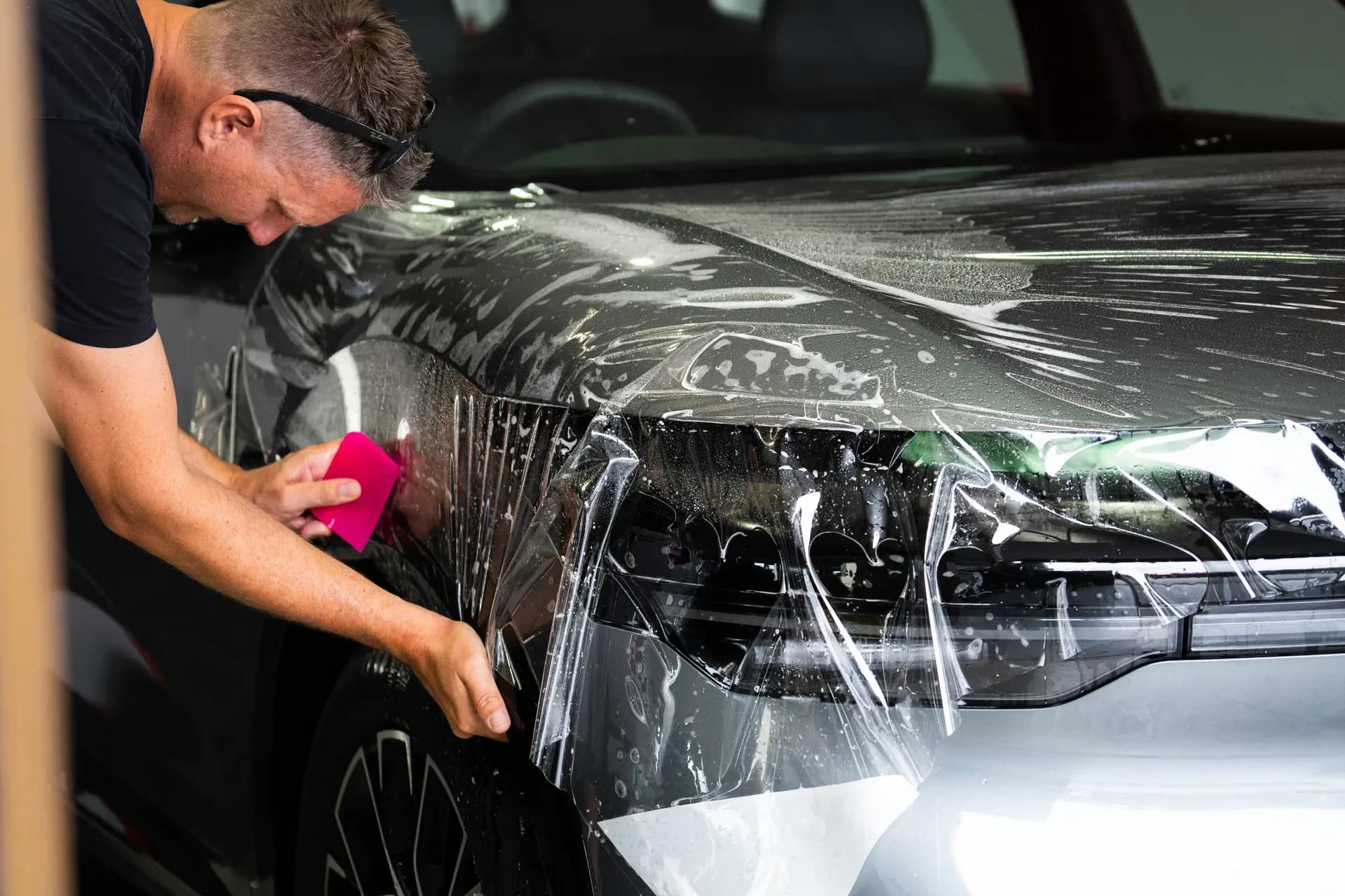 Wrap Culture installer applying paint protection film to a vehicle's front bumper and headlight